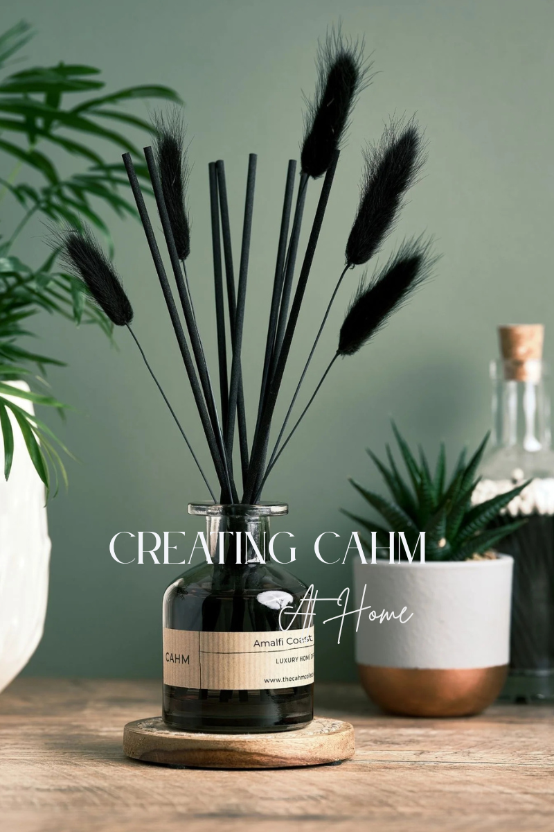 A bottle labeled 'Amalfi Coast' with decorative black plants on a wooden surface, featuring the text 'Creating Calm At Home'.